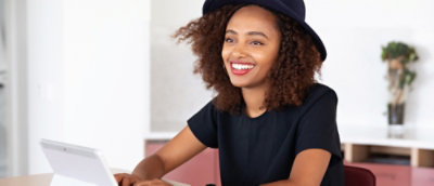A person with curly hair wearing a hat and a black shirt.