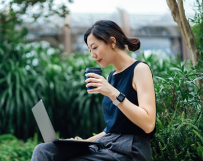 A person holding a coffee cup and a laptop outdoors.