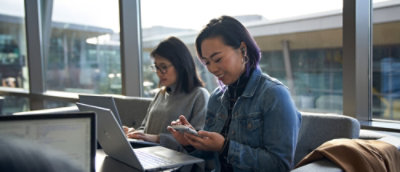 A woman wearing glasses and a gray sweater looking at her phone.