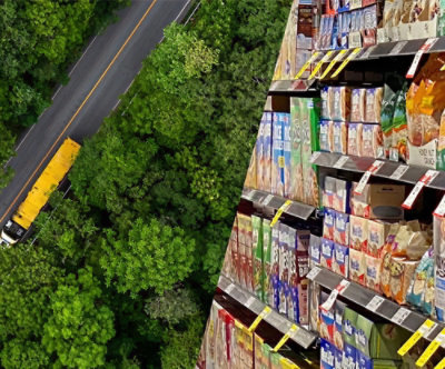 Aerial view of a supermarket aisle with shelves and a yellow school bus driving along a jungle road outside.
