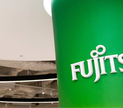 Close-up of a green Fujitsu sign with an out-of-focus interior background.