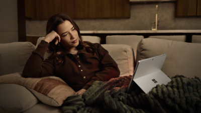 A person sitting on a sofa in a burgundy shirt with a Platinum Surface Pro.