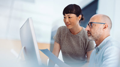 A man and woman sitting at a table and discussing something on a monitor screen.
