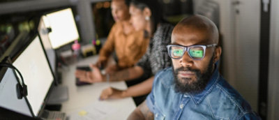 Person working at a computer with colleagues in the background.