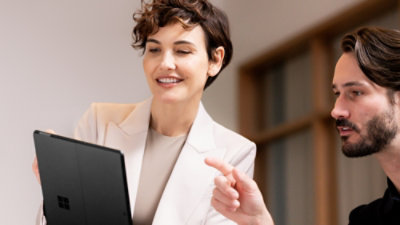 Two people reviewing a tablet, one pointing at the screen in an office setting.