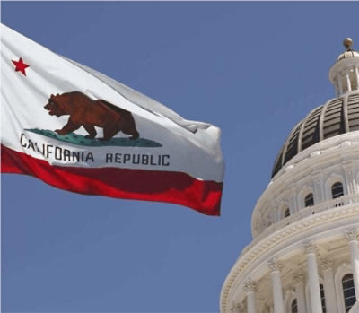 A flag with the text CALIFORNIA REPUBLIC and a bear flying in front of a white building under a blue sky.