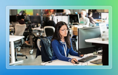 A person wearing a blue sweater sitting at a desk using a computer.