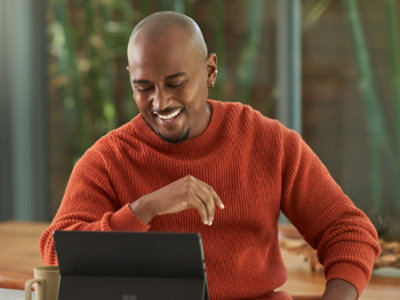 A person in a cozy orange sweater smiles while using a tablet at a table.