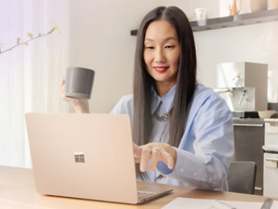 A woman holding a cup and looking at a laptop.