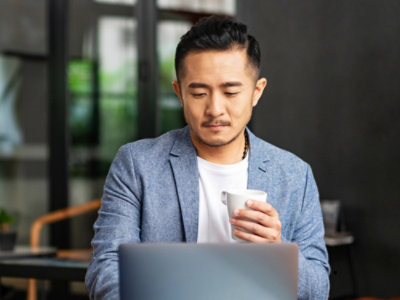 A man holding a cup of coffee looking at a laptop.