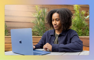 A person uses a laptop outdoors, surrounded by plants.
