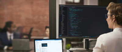 一個人坐在桌前，使用兩台顯示器工作，一台顯示文件，另一台顯示設計元素。