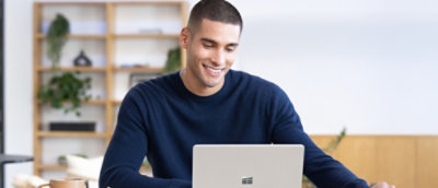 Ein Mann mit blauem Pullover, der auf einen Laptop blickt und lächelt