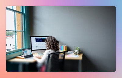 2 台のノート PC のある机に向かって座っている女性