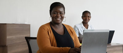 Two women sitting beside laptop and looking forward in the office environment