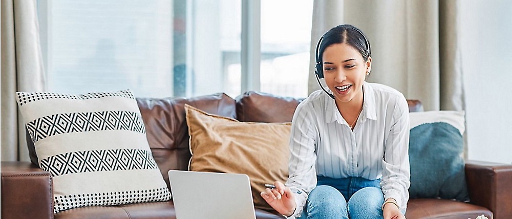 Een stralende vrouw zit op een bank met een laptop en voert een gesprek in een heldere, moderne huiskamer.
