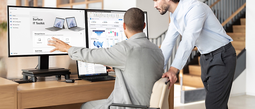 Zwei Geschäftsleute diskutieren über Computerbildschirme in einer modernen Büroumgebung.