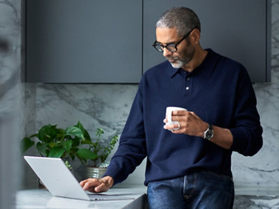 Osoba, která drží šálek při používání notebooku s rostlinou v pozadí.