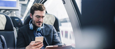 גבר מרכיב משקפיים ואוזניות, מביט בטלפון החכם שלו הזמן שהוא יושב ברכבת.