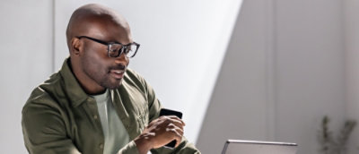 A man wearing glasses and a green shirt looking at a laptop.