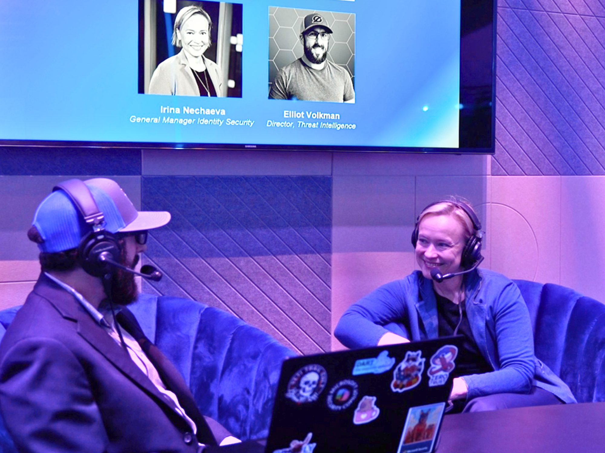 Two people wearing headphones in a studio conversation, seated with a laptop on a table.