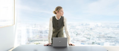 A woman smiling at a laptop while wearing glasses and white earbuds.