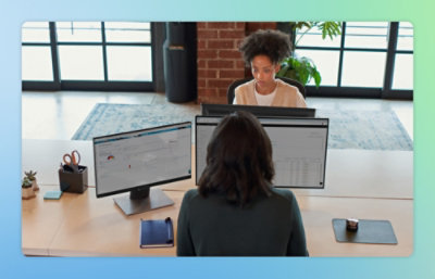 Две женщины сидят друг напротив друга за столом и работают за компьютерами.