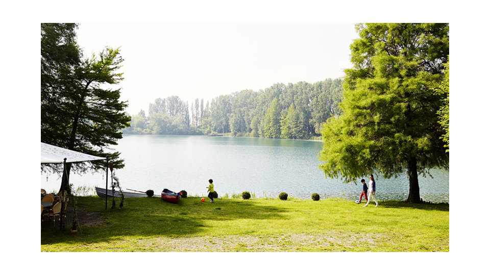 A serene lakeside scene with lush greenery and a shaded area with chairs