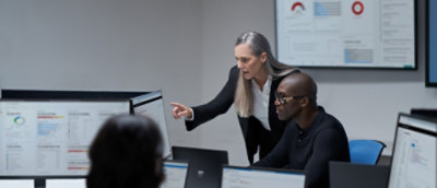 A woman pointing at a computer screen near a whiteboard with red circles and blue squares.