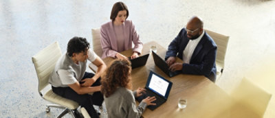 A group of people sitting around a table with laptops.
