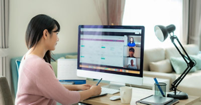 Una donna con una felpa rosa partecipa a una conferenza video dal computer di casa. 