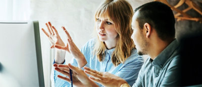 Una donna e un uomo seduti indicano lo schermo di un computer, impegnati in una discussione.