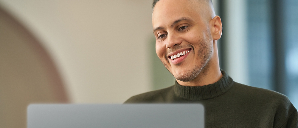 A smiling bald man working on a laptop in a modern office setting.