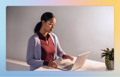 En kvinde i en sweater, der skriver på en bærbar computer, mens hun sidder ved et skrivebord.