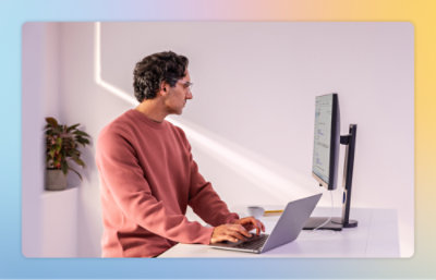 En mand i en rød sweater sidder ved et skrivebord og bruger en bærbar computer.