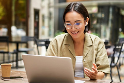 En kvinde med briller og hovedtelefoner, der sidder ved et bord og bruger en bærbar computer.