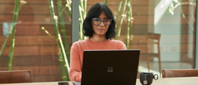 A woman wearing glasses and a pink shirt sitting at a desk with a laptop.