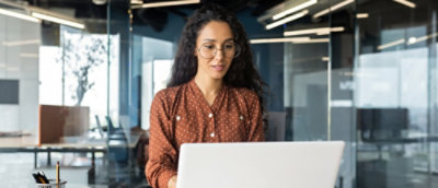 A woman wearing glasses looking at a laptop.