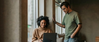 A woman wearing headphones and looking at a laptop next to a man in a green shirt.