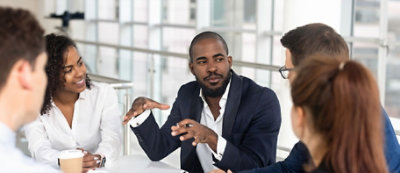 Un gruppo di quattro professionisti discutono intorno a un tavolo, con un uomo che gesticola mentre parla.