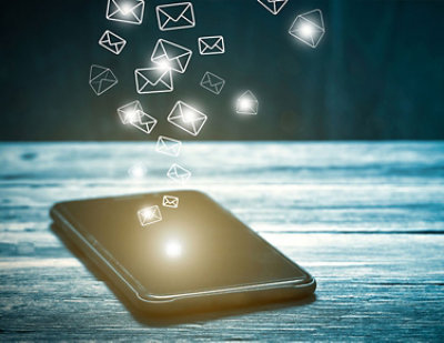 A smartphone on a wooden surface with glowing email icons floating above it, symbolizing the receipt or sending of messages.
