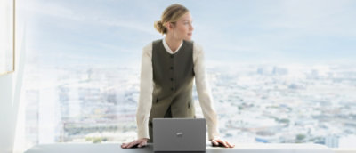 Egy nő áll egy laptop előtt irodai környezetben, és félrenéz