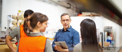 גבר בגיל העמידה מחזיק טאבלט ומדבר אל קבוצת עובדים שלובשים וסט בטיחות