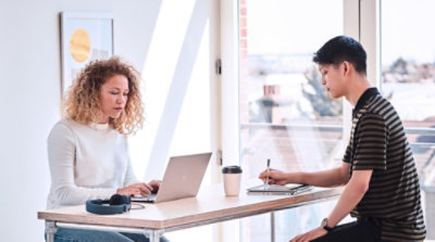 Two people working at a high-top table with a laptop and a tablet