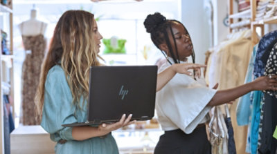 Two workers holding a laptop and looking at clothing in a retail store