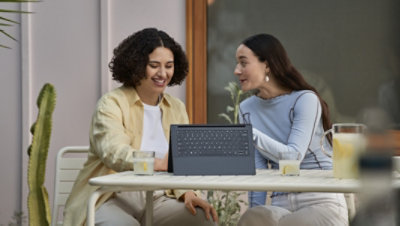 Two people sitting outside using a laptop flipped into tablet mode.