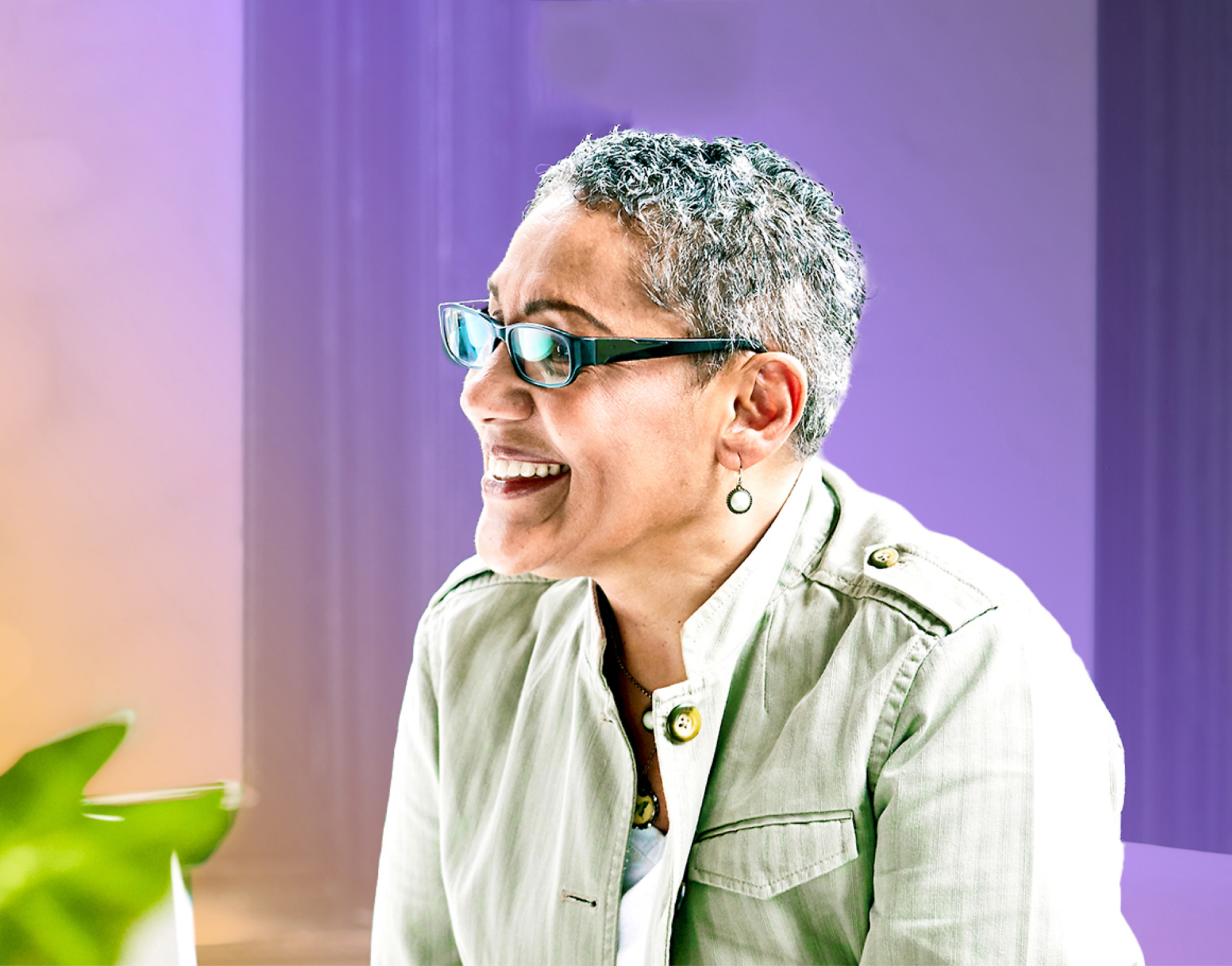 Mature woman with short gray hair and glasses, laughing, wearing a light green jacket, 