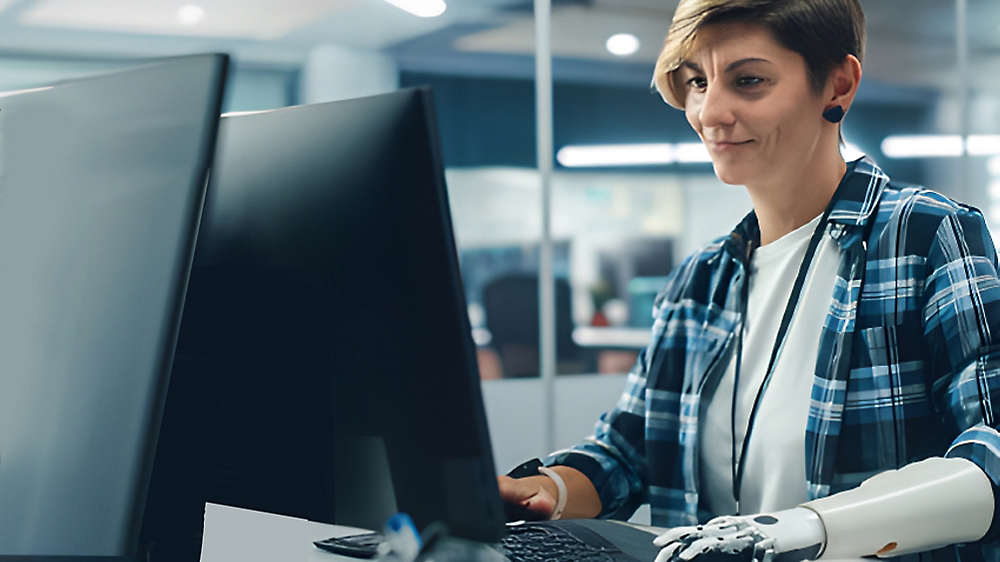 Eine Frau mit einer Armprothese, die konzentriert an einem Computer in einer modernen Büroumgebung arbeitet.