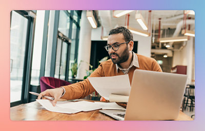 Persoon die op een laptop werkt aan een bureau en documenten bekijkt in een moderne kantooromgeving.