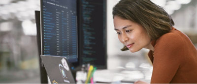 Person working on a laptop with additional monitors displaying code in an office environment.